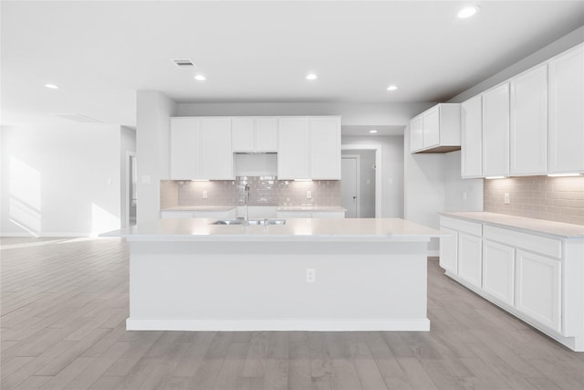 kitchen with white cabinets, tasteful backsplash, a sink, a kitchen island with sink, and light wood-type flooring