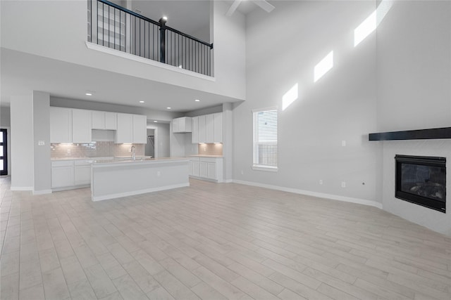 unfurnished living room with a glass covered fireplace, light wood-style floors, baseboards, a high ceiling, and a sink