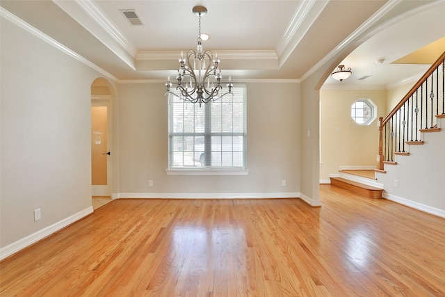 spare room featuring visible vents, arched walkways, wood finished floors, a raised ceiling, and a notable chandelier