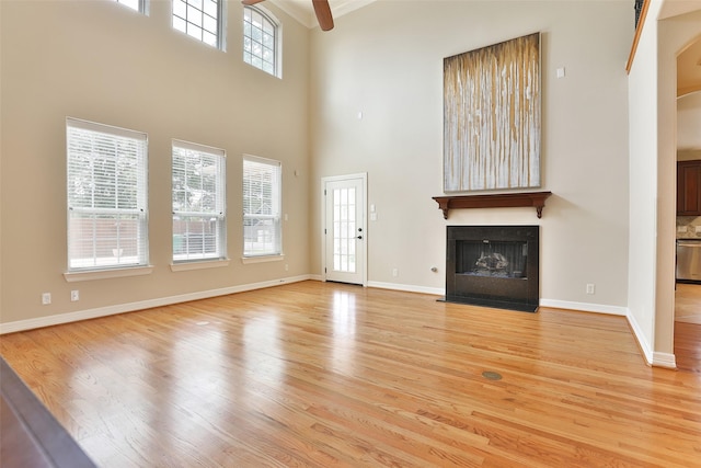 unfurnished living room with a ceiling fan, a high ceiling, a large fireplace, and light wood finished floors