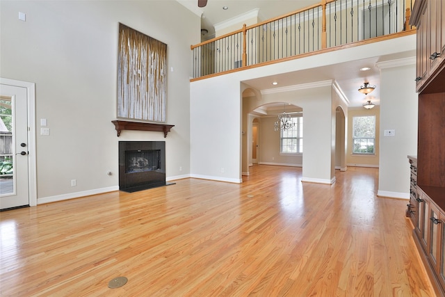 unfurnished living room featuring arched walkways, a fireplace with flush hearth, a towering ceiling, and light wood-style flooring