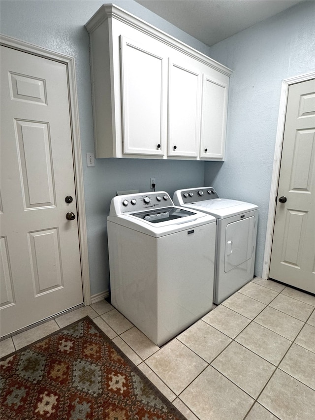 washroom featuring cabinet space, light tile patterned flooring, a textured wall, and washer and clothes dryer