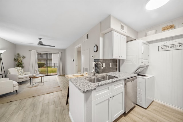 kitchen with visible vents, stainless steel dishwasher, stacked washer / drying machine, a sink, and open floor plan