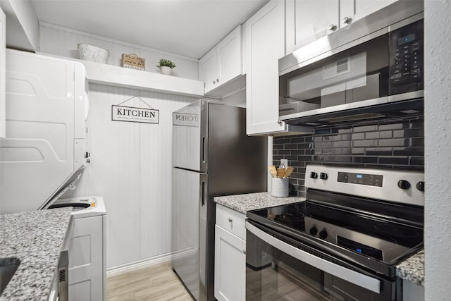 kitchen featuring white cabinets, tasteful backsplash, stacked washing maching and dryer, stainless steel appliances, and light wood-type flooring