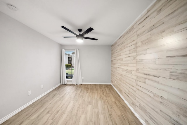 spare room featuring an accent wall, wood finished floors, baseboards, wooden walls, and a ceiling fan
