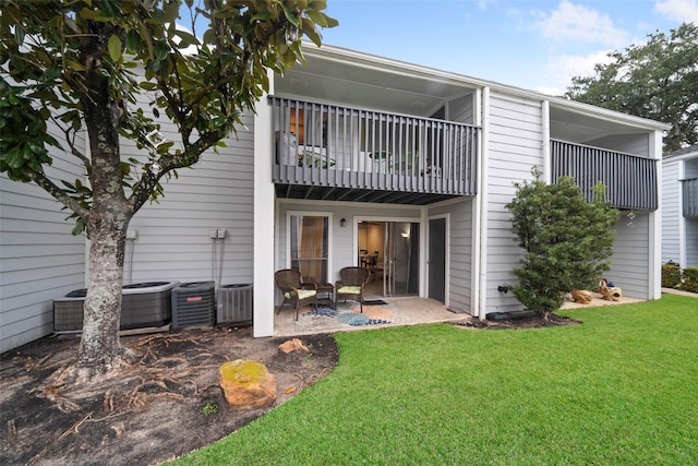 rear view of property featuring central AC unit, a yard, a patio area, and a balcony