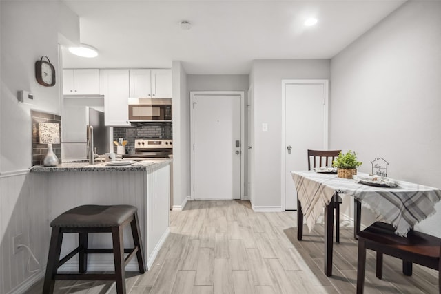 kitchen with a peninsula, white cabinets, light wood finished floors, backsplash, and stainless steel appliances