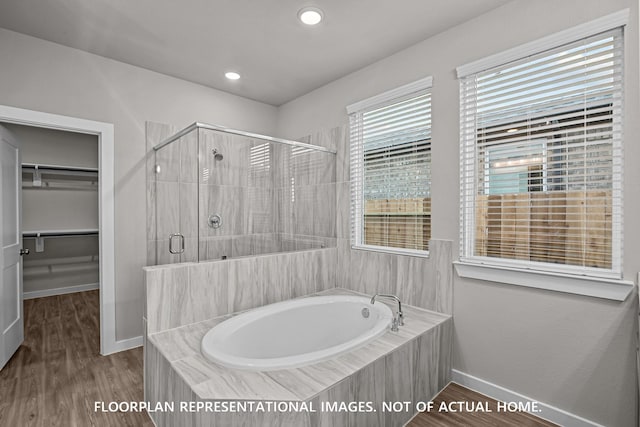 bathroom with wood finished floors, baseboards, a bath, a spacious closet, and a stall shower