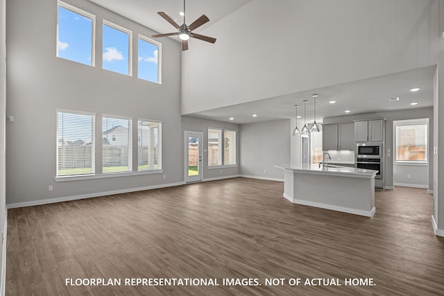 unfurnished living room with baseboards, ceiling fan, a sink, and dark wood-type flooring