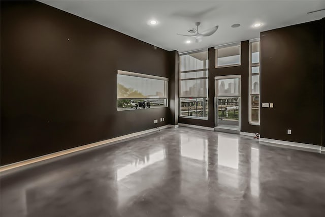 empty room featuring ceiling fan, finished concrete floors, a towering ceiling, baseboards, and recessed lighting