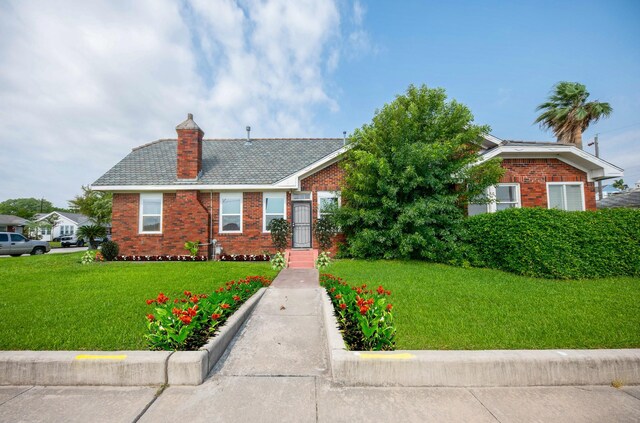 view of front of home featuring a chimney, brick siding, and a front yard