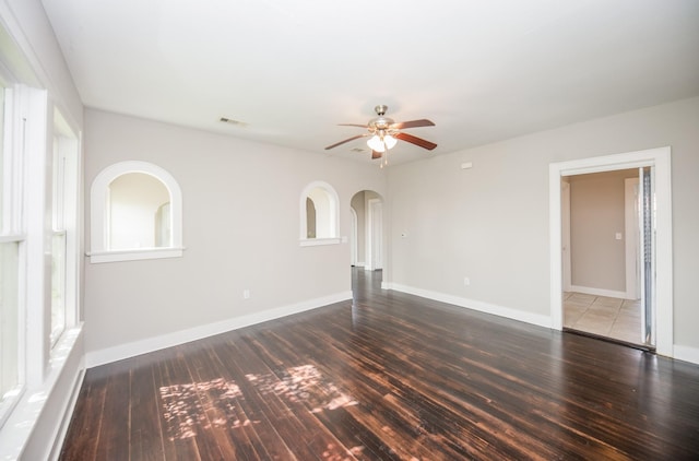 unfurnished living room with baseboards, a ceiling fan, arched walkways, and wood finished floors