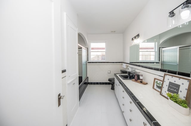 full bathroom featuring vanity, wainscoting, tile walls, tile patterned floors, and a shower with shower door