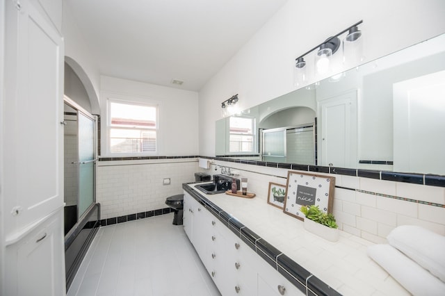 bathroom with vanity, wainscoting, toilet, tile walls, and a shower with shower door