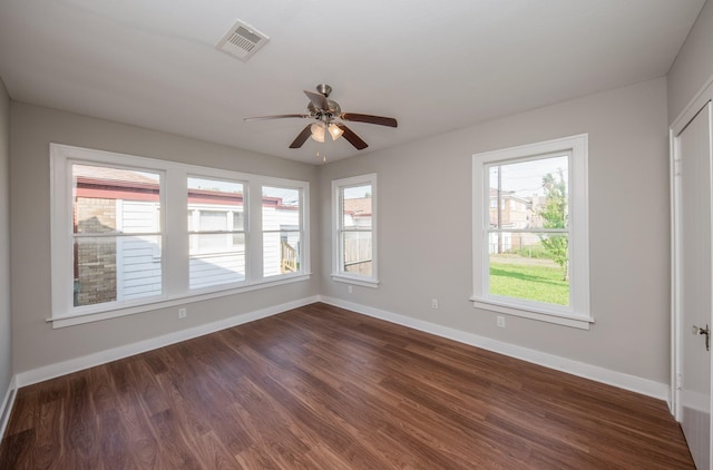 spare room featuring baseboards, ceiling fan, dark wood-type flooring, and visible vents