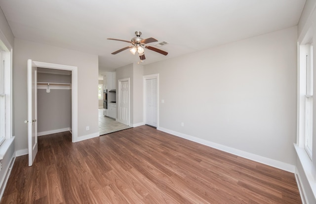 unfurnished bedroom featuring visible vents, wood finished floors, two closets, baseboards, and ceiling fan