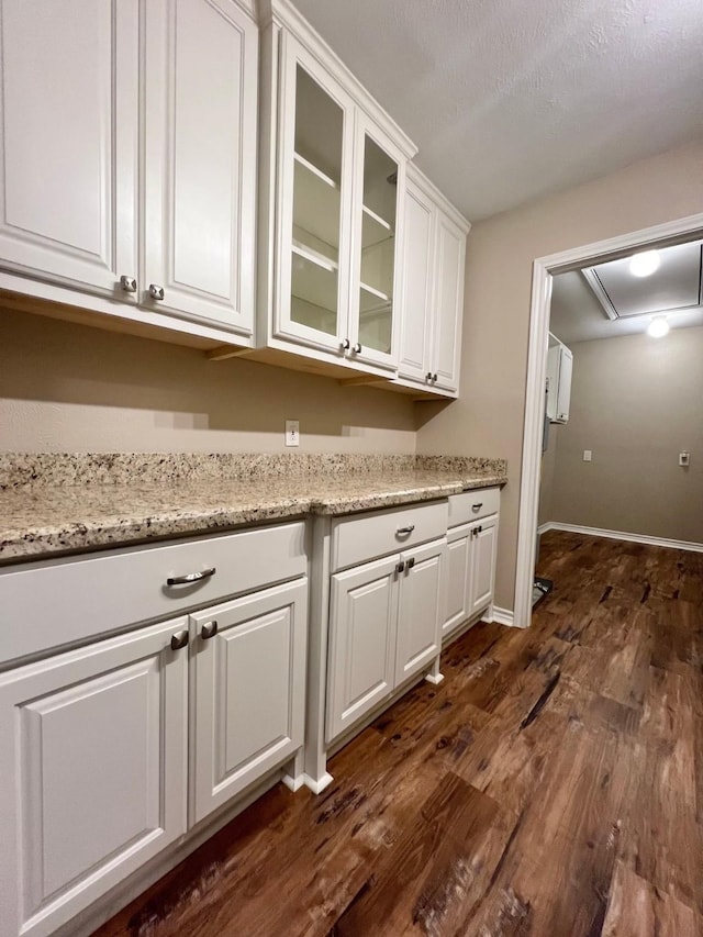 interior space featuring white cabinets, light stone countertops, baseboards, dark wood-type flooring, and glass insert cabinets