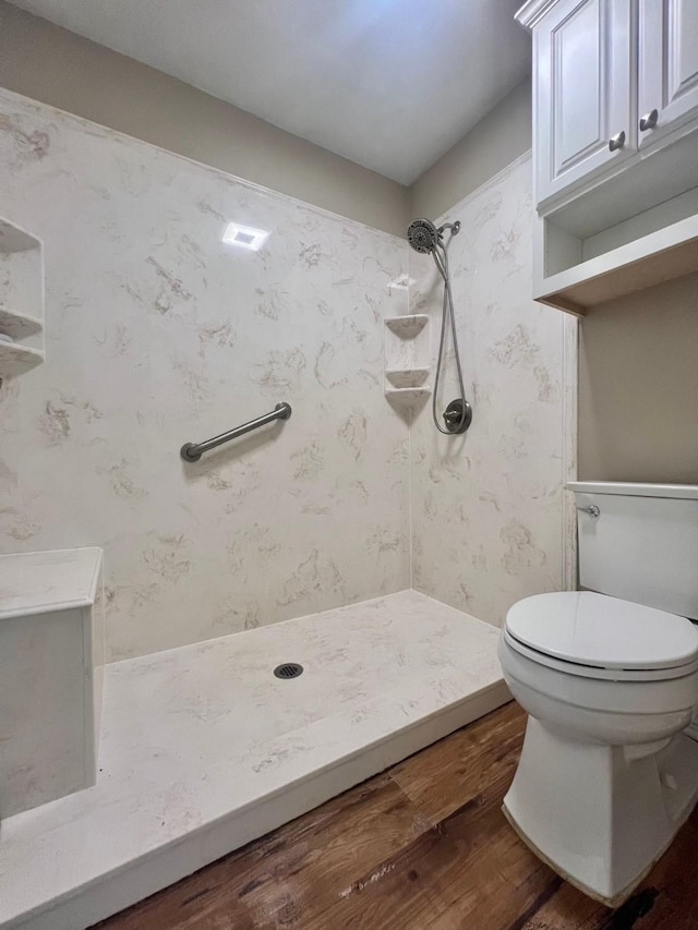 bathroom featuring toilet, tiled shower, and wood finished floors
