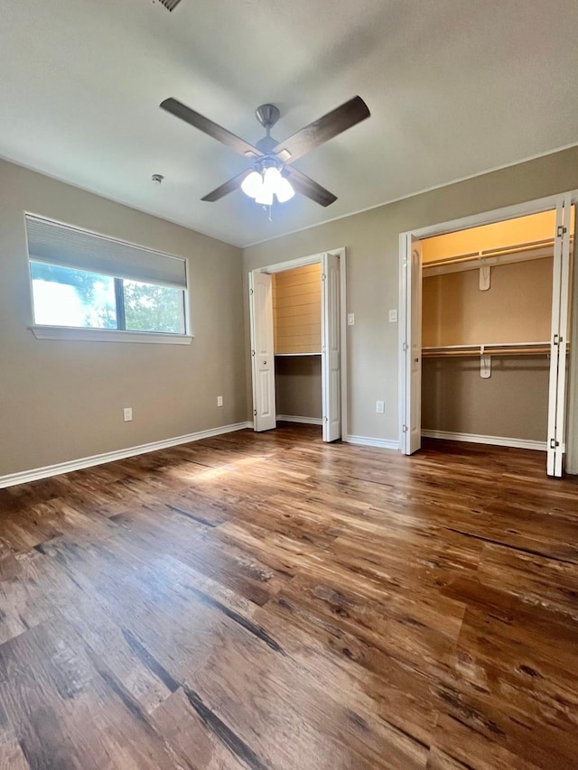 unfurnished bedroom featuring baseboards, a ceiling fan, two closets, and wood finished floors