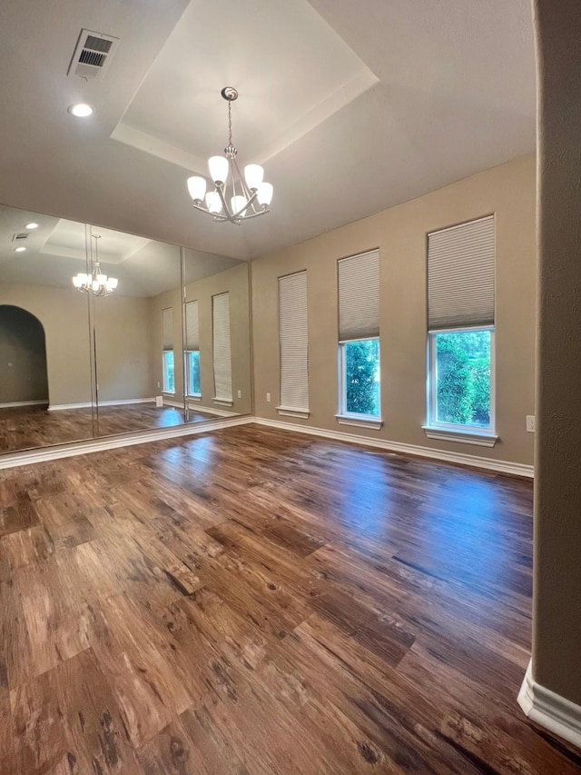 interior space with baseboards, an inviting chandelier, wood finished floors, and a raised ceiling