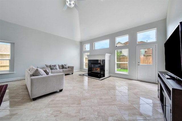 living area with baseboards, a ceiling fan, a fireplace, and high vaulted ceiling