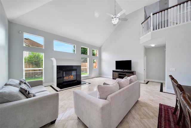 living area with high vaulted ceiling, a glass covered fireplace, plenty of natural light, and ceiling fan
