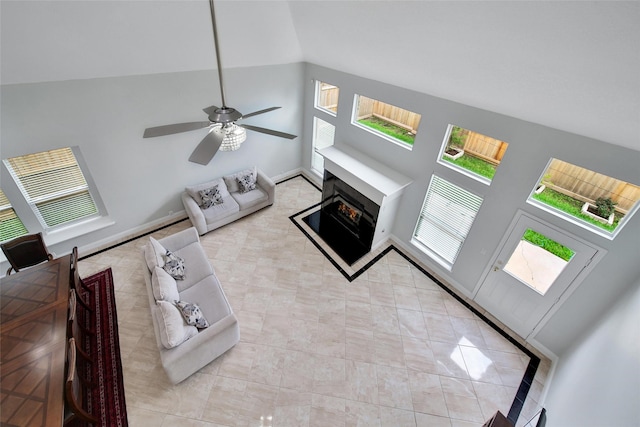 living room featuring vaulted ceiling, ceiling fan, and a lit fireplace