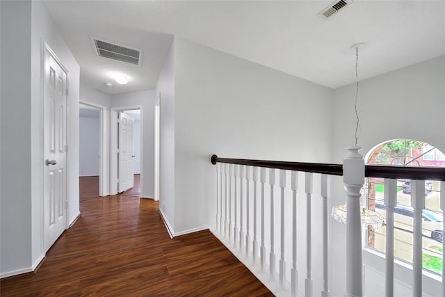 hall with visible vents, baseboards, wood finished floors, and an upstairs landing