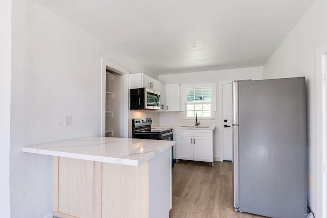 kitchen featuring appliances with stainless steel finishes, a sink, light wood finished floors, a peninsula, and white cabinetry
