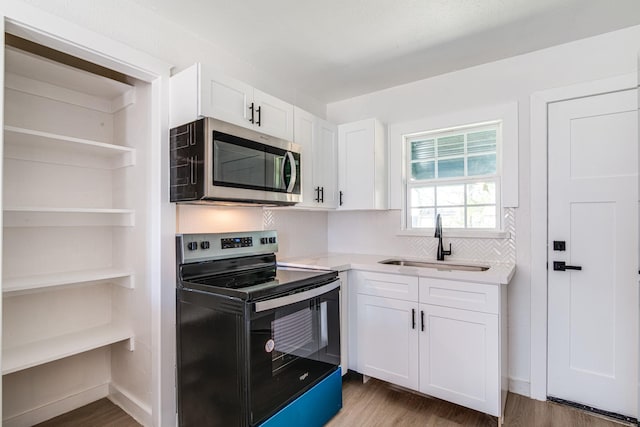 kitchen featuring appliances with stainless steel finishes, wood finished floors, a sink, light countertops, and white cabinets