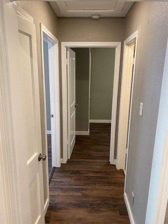 corridor featuring dark wood-style flooring, baseboards, a textured wall, and attic access