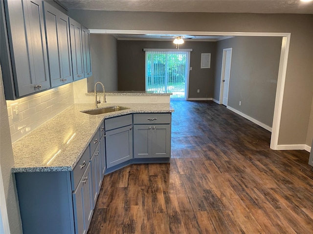 kitchen with a peninsula, dark wood finished floors, a sink, and tasteful backsplash