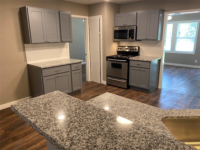 kitchen with appliances with stainless steel finishes, tasteful backsplash, light stone countertops, gray cabinetry, and baseboards