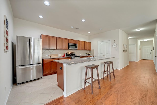 7908 Beryl Ct, Texas City, TX 77591 - kitchen with decorative backsplash, a center island with sink, a kitchen bar, brown cabinets, and stainless steel appliances
