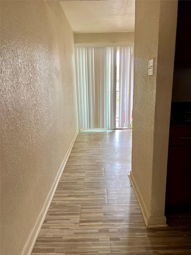hall with baseboards, a textured wall, a textured ceiling, and wood finished floors