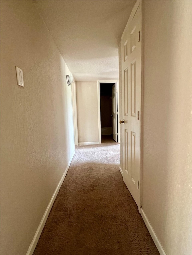hall featuring baseboards, a textured wall, and carpet