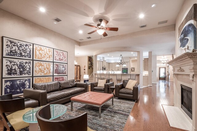 living room featuring wood-type flooring, visible vents, ceiling fan with notable chandelier, and a high end fireplace