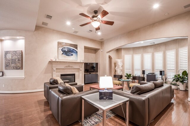 living room with ceiling fan, visible vents, arched walkways, a fireplace, and wood finished floors