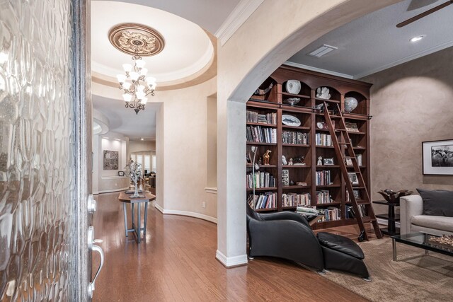 sitting room featuring crown molding, wood-type flooring, an inviting chandelier, baseboards, and arched walkways