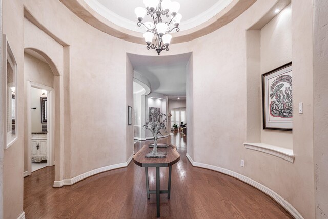 hallway featuring arched walkways, baseboards, a chandelier, and wood finished floors