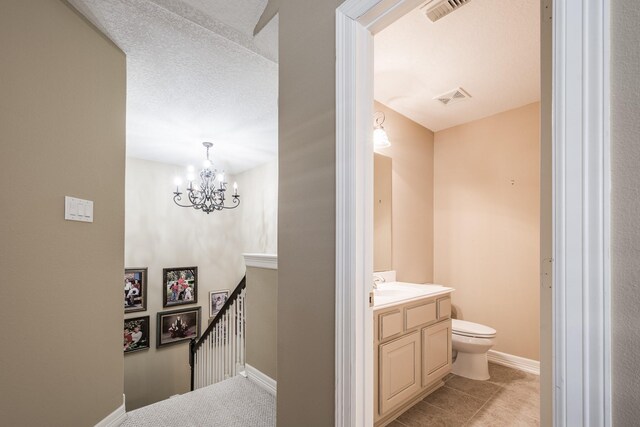 half bath with visible vents, vanity, baseboards, toilet, and an inviting chandelier