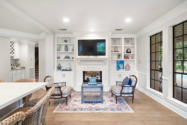 32743 Weybridge St, Fulshear, TX 77441 - living area with a large fireplace, light wood-type flooring, crown molding, built in features, and recessed lighting