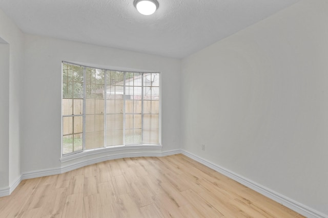 empty room featuring baseboards, light wood-type flooring, and a textured ceiling