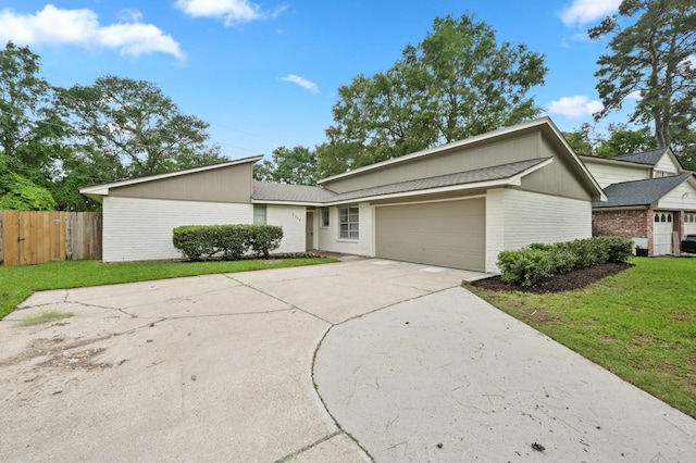 mid-century modern home featuring driveway, a front yard, a garage, brick siding, and fence