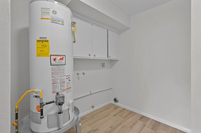 laundry area featuring cabinet space, light wood-style flooring, water heater, electric dryer hookup, and baseboards