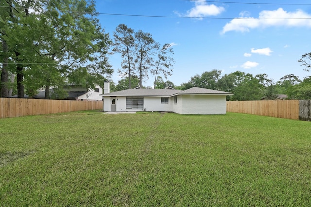 rear view of house with a fenced backyard, a chimney, and a yard