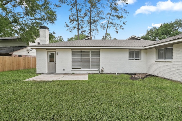 rear view of house featuring a chimney, a lawn, a patio area, brick siding, and fence