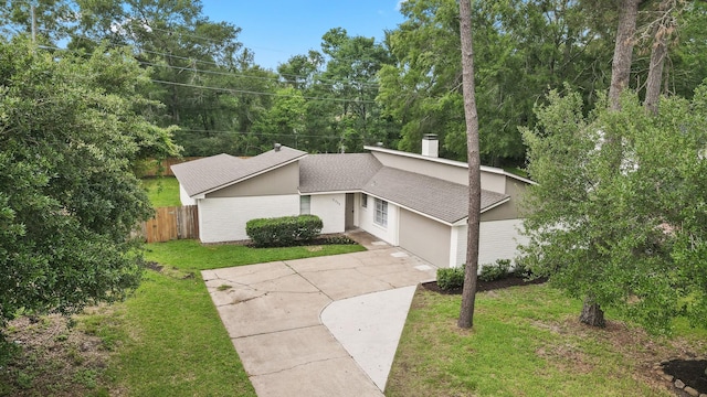 view of home's exterior featuring a chimney, a yard, fence, concrete driveway, and a shingled roof