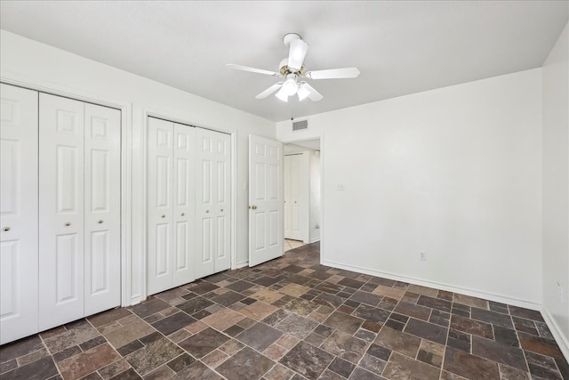 3139 Fm 1406, Winnie, TX 77665 - unfurnished bedroom with visible vents, two closets, baseboards, ceiling fan, and stone finish flooring