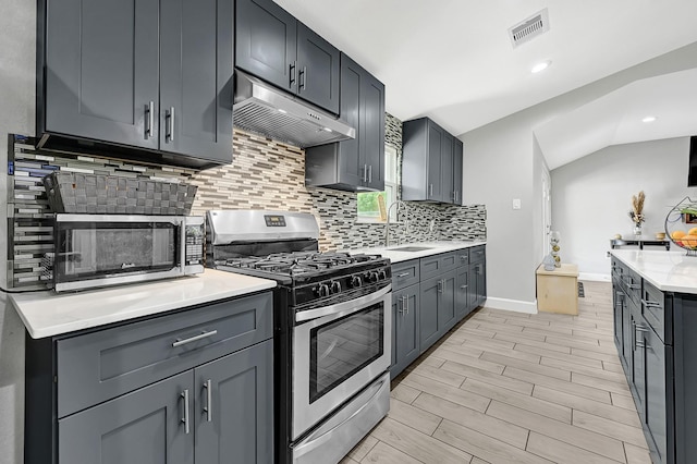 kitchen featuring visible vents, under cabinet range hood, a sink, backsplash, and stainless steel appliances